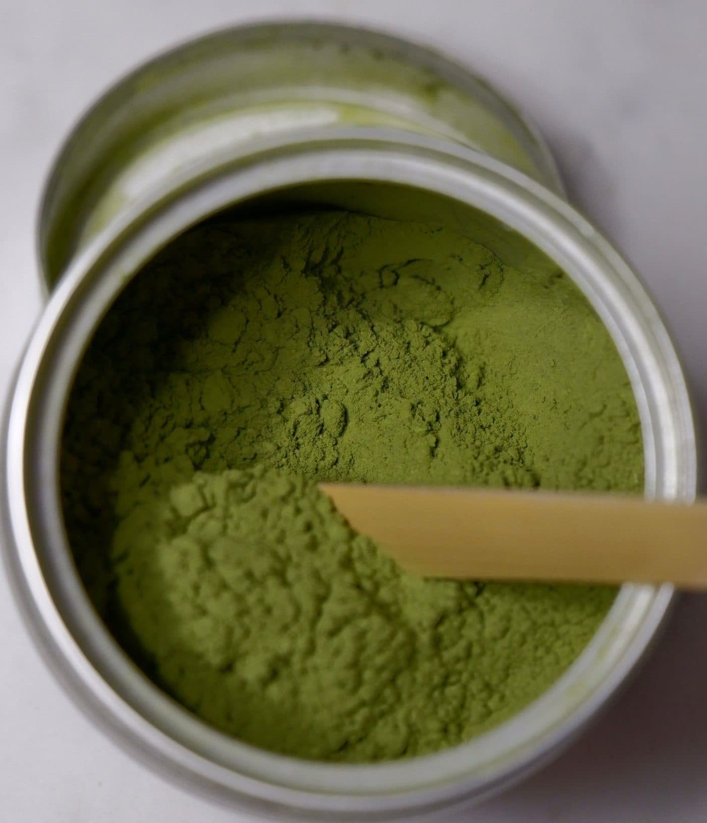 Matcha en polvo dentro de una lata abierta, con una cuchara de bambú