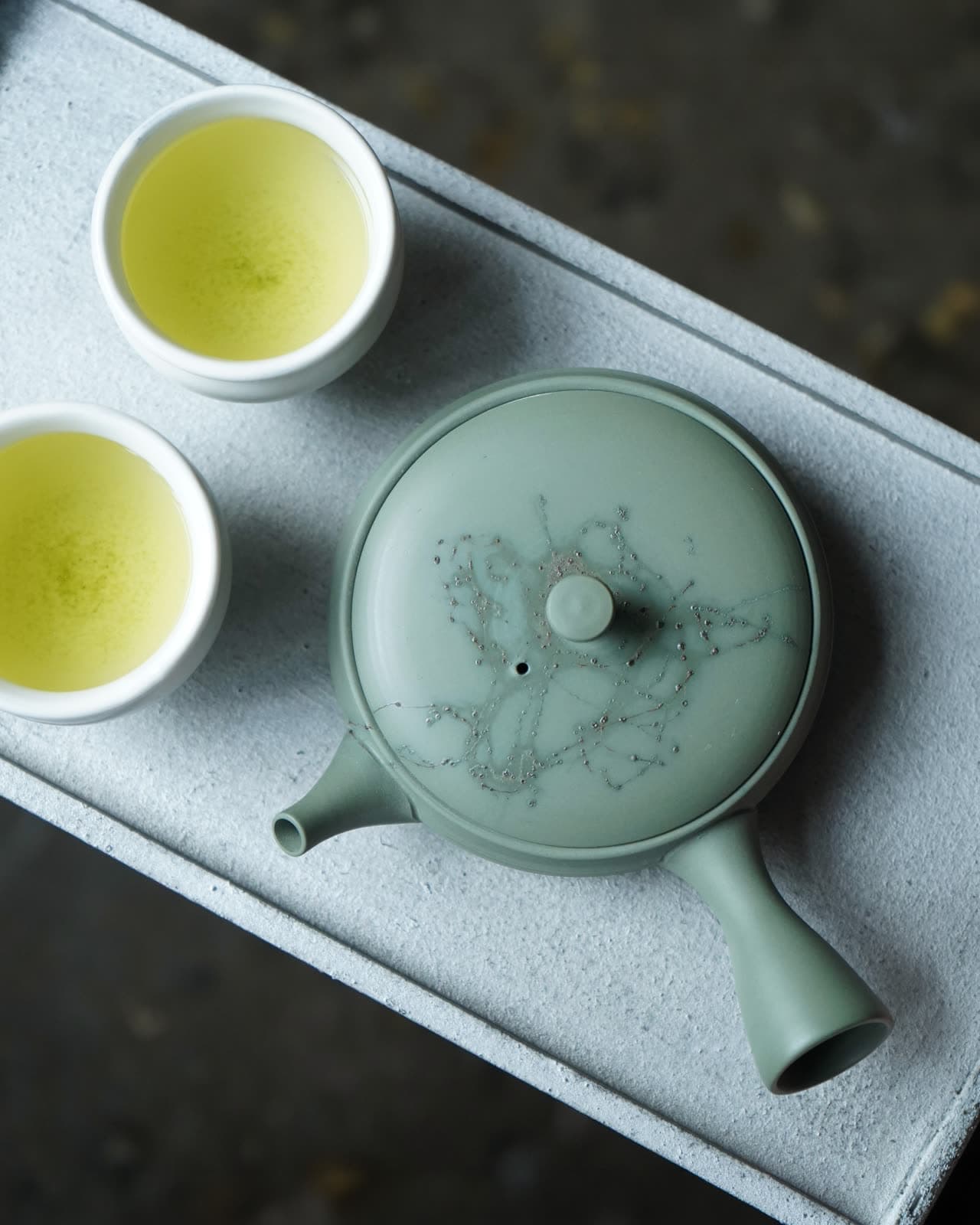 Kyusu de arcilla verde visto desde arriba, junto a dos tazas de té verde