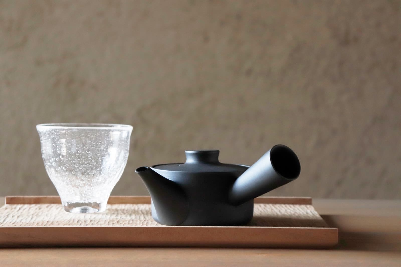 Kyusu negro sobre una bandeja de madera junto a un vaso de vidrio